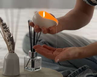 a woman is pouring melted massage candle in her hand